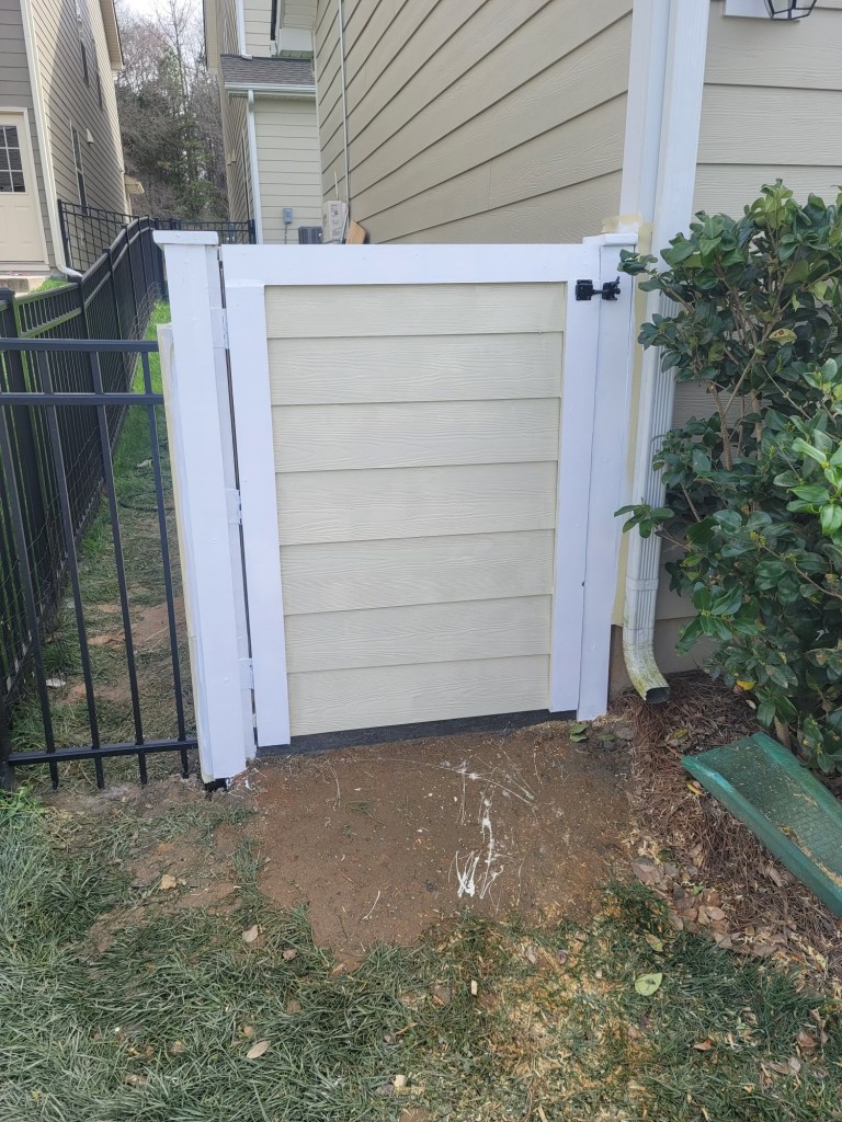 Trash can enclosure at the side of a house in a residential neighborhood. Beige and Whtie with a black lock.