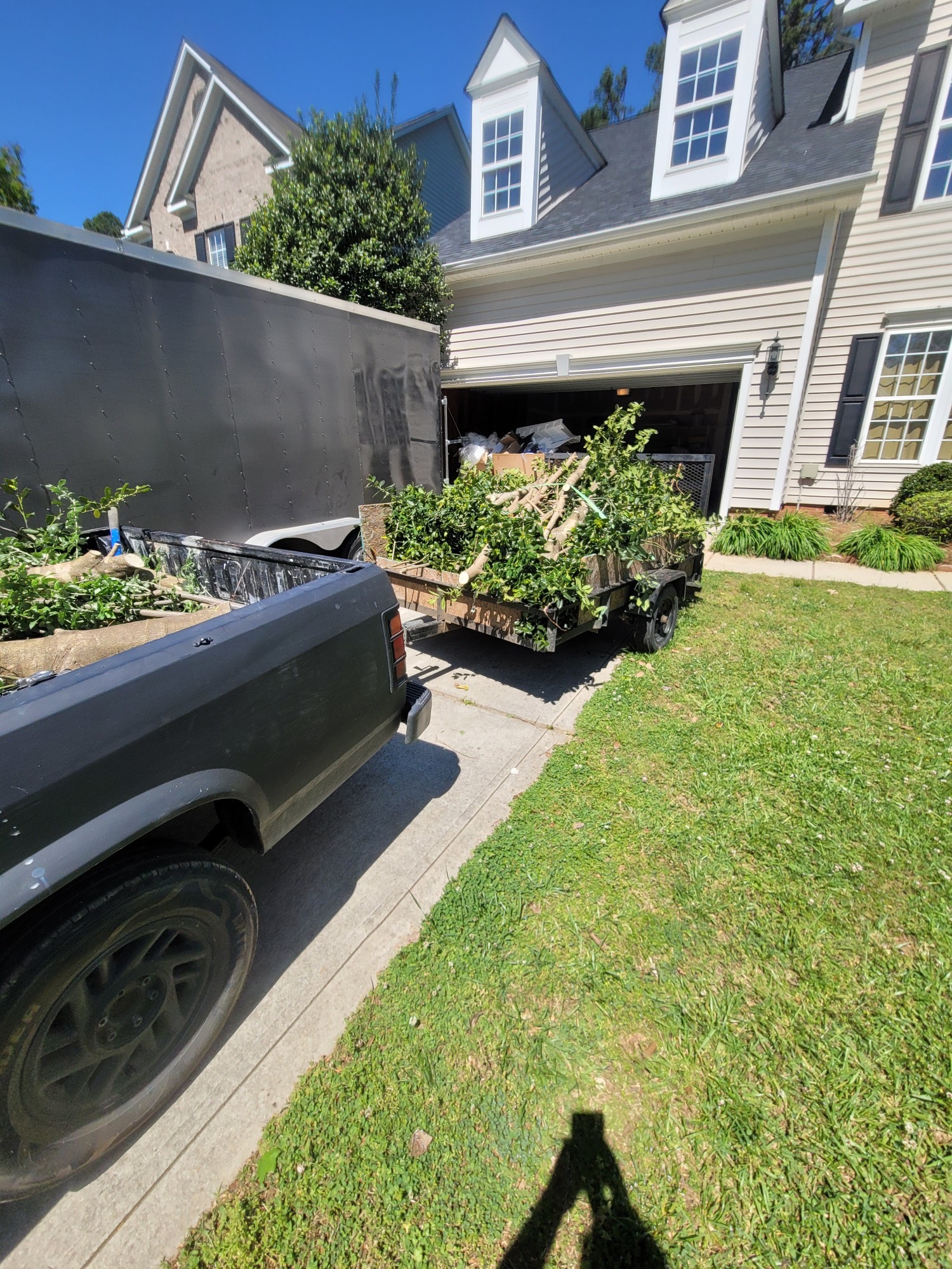 Pickup truck and trailer loaded with yard debris during a residential clean-up in front of a home.
