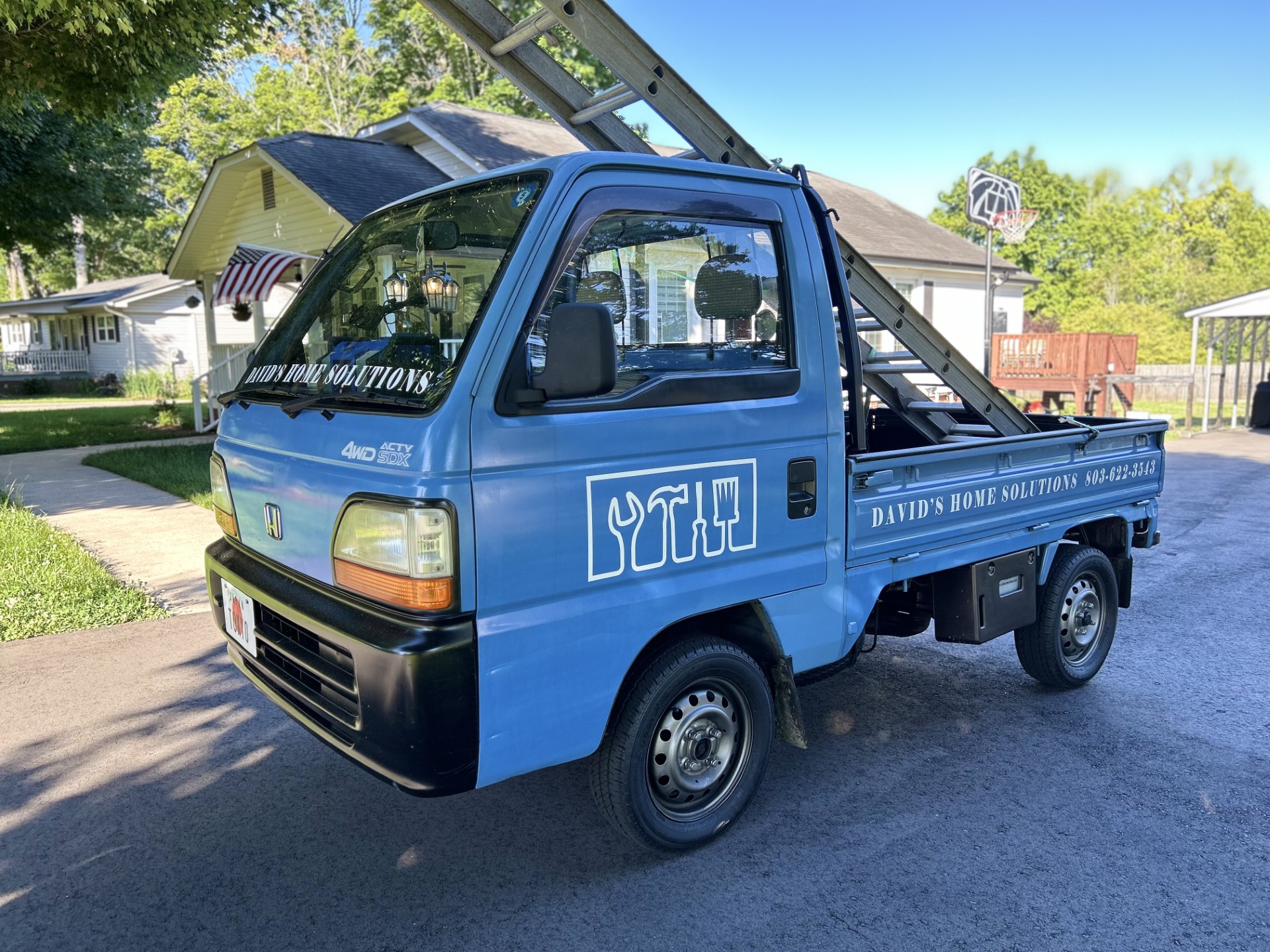 This is an image of the mini truck that Dave uses for his work. It has the company logo on it and it's blue.